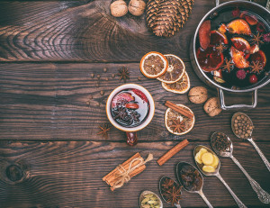 mulled wine and ingredients in iron spoons for making a drink on a brown wooden background, empty space on the left